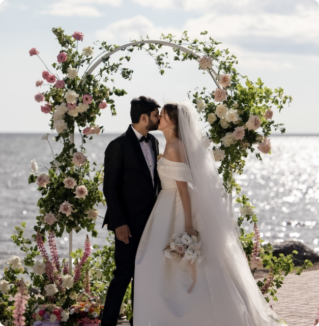A couple beneath a floral mandap archway by the sea